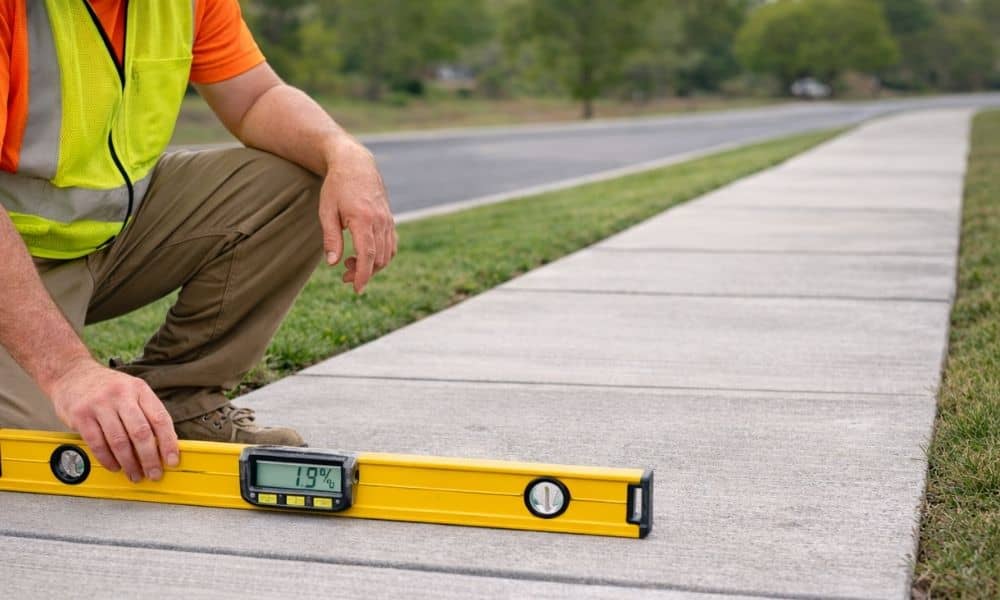 Construction worker measuring sidewalk cross slope with digital level to verify ADA compliance limits