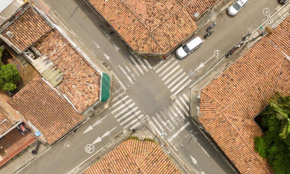 Top-down aerial view of a four-way road intersection showing crosswalks, lane markings, and traffic flow